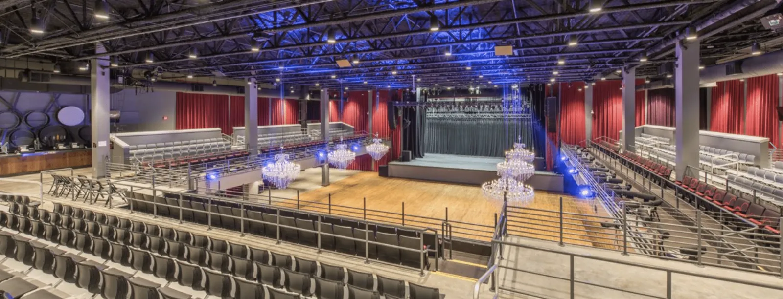 Spacious modern auditorium with tiered seating, chandeliers, and a large stage under blue ceiling lights.