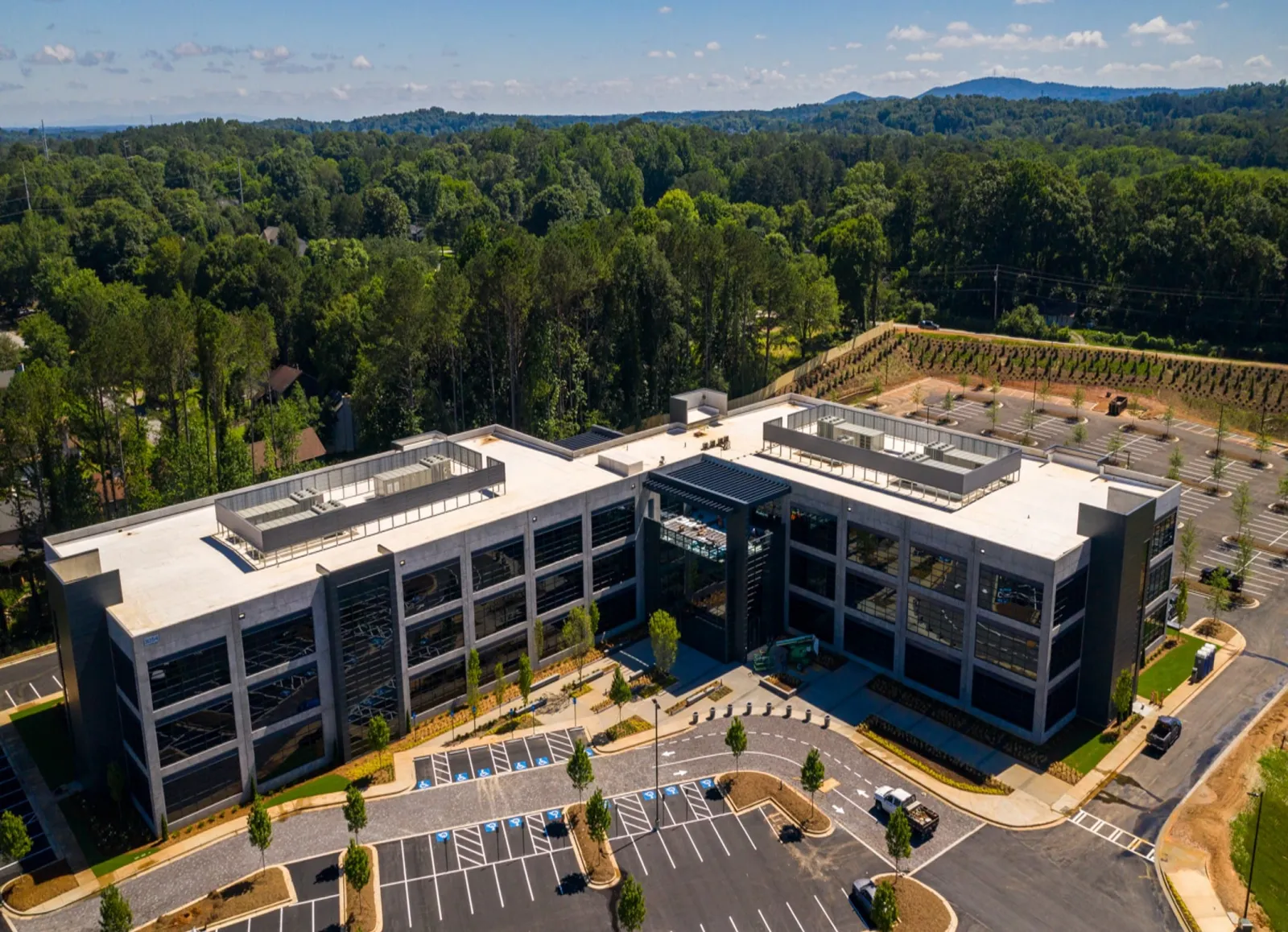 Modern three-story office building surrounded by trees with large parking lot and clear blue sky