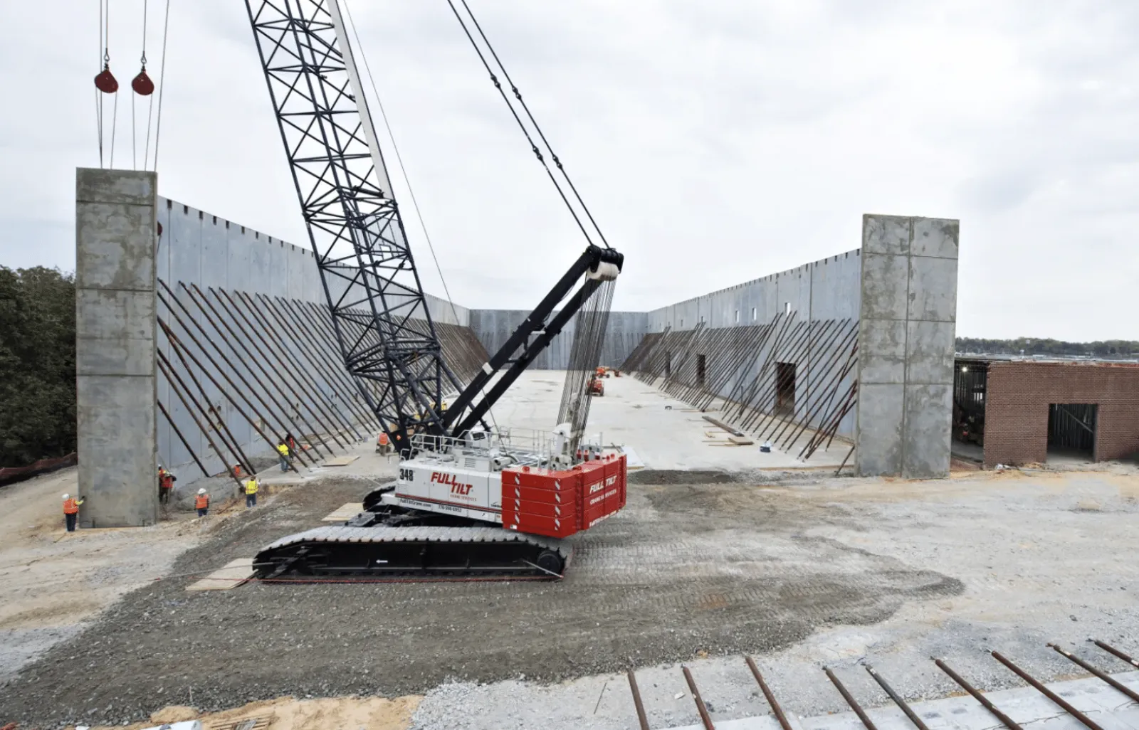 Large crane and workers constructing a massive concrete structure at a construction site under cloudy sky