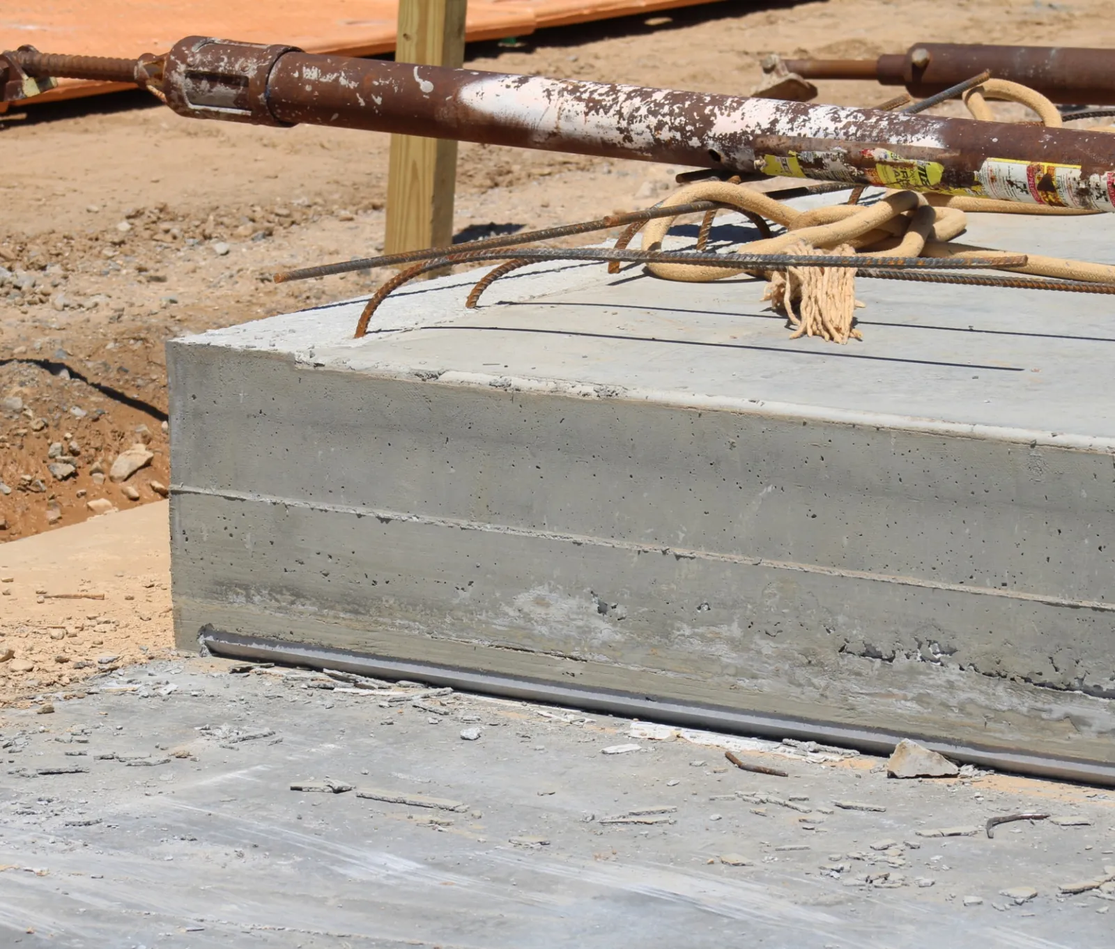 Close-up of concrete foundation slab with construction rebar and rusted metal pipe at a building site.
