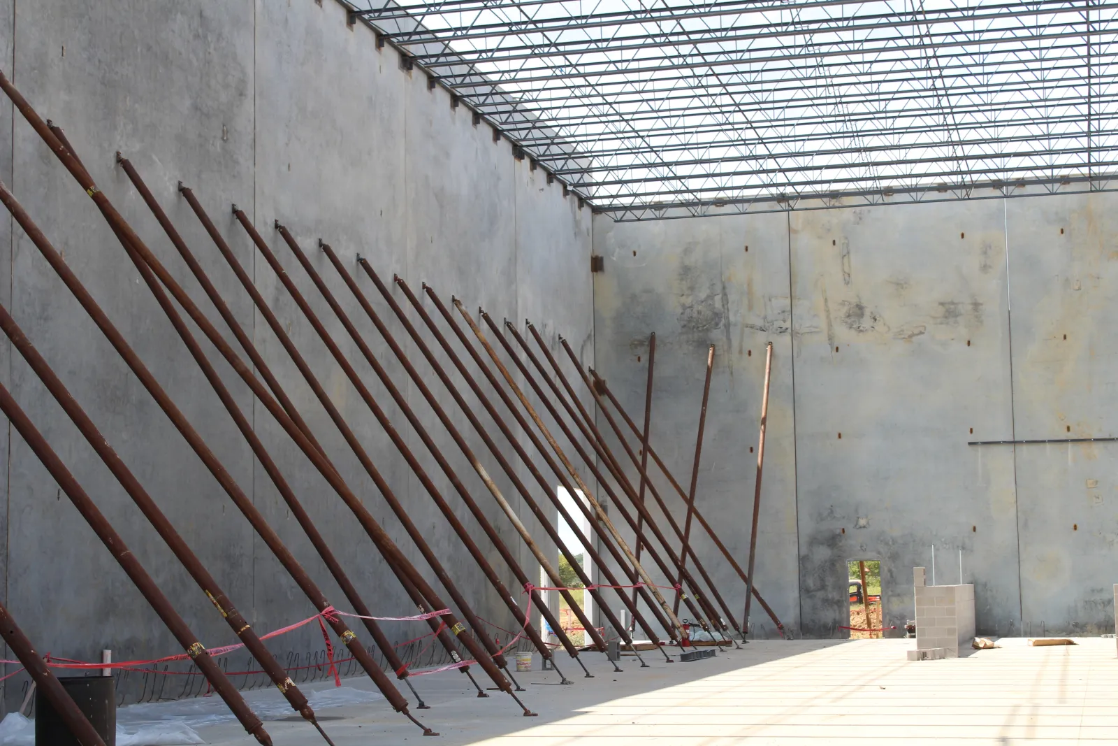 Construction site with concrete walls supported by angled steel braces and a large open ceiling grid.