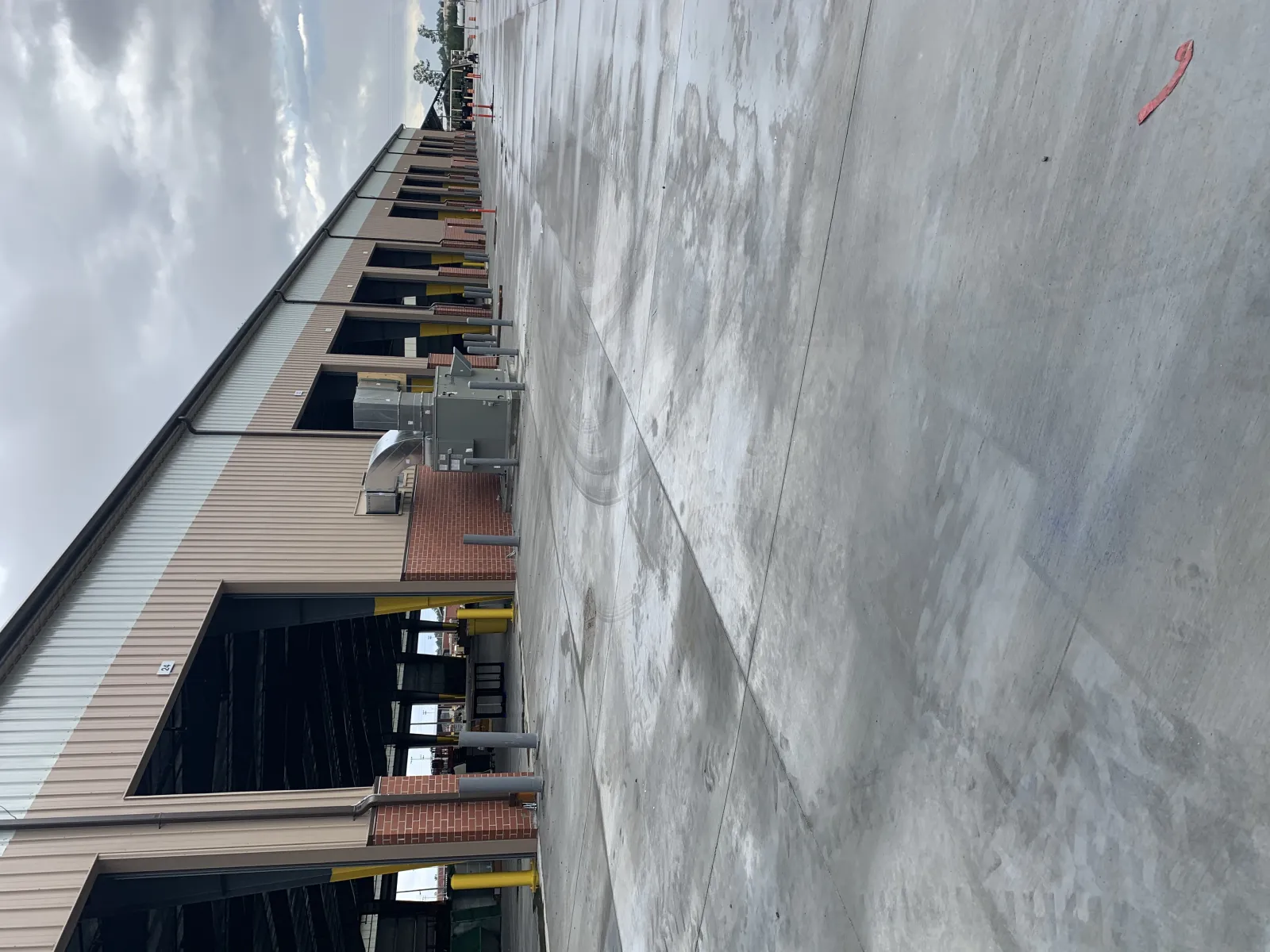 Wet concrete loading dock area beside industrial warehouse building under cloudy sky