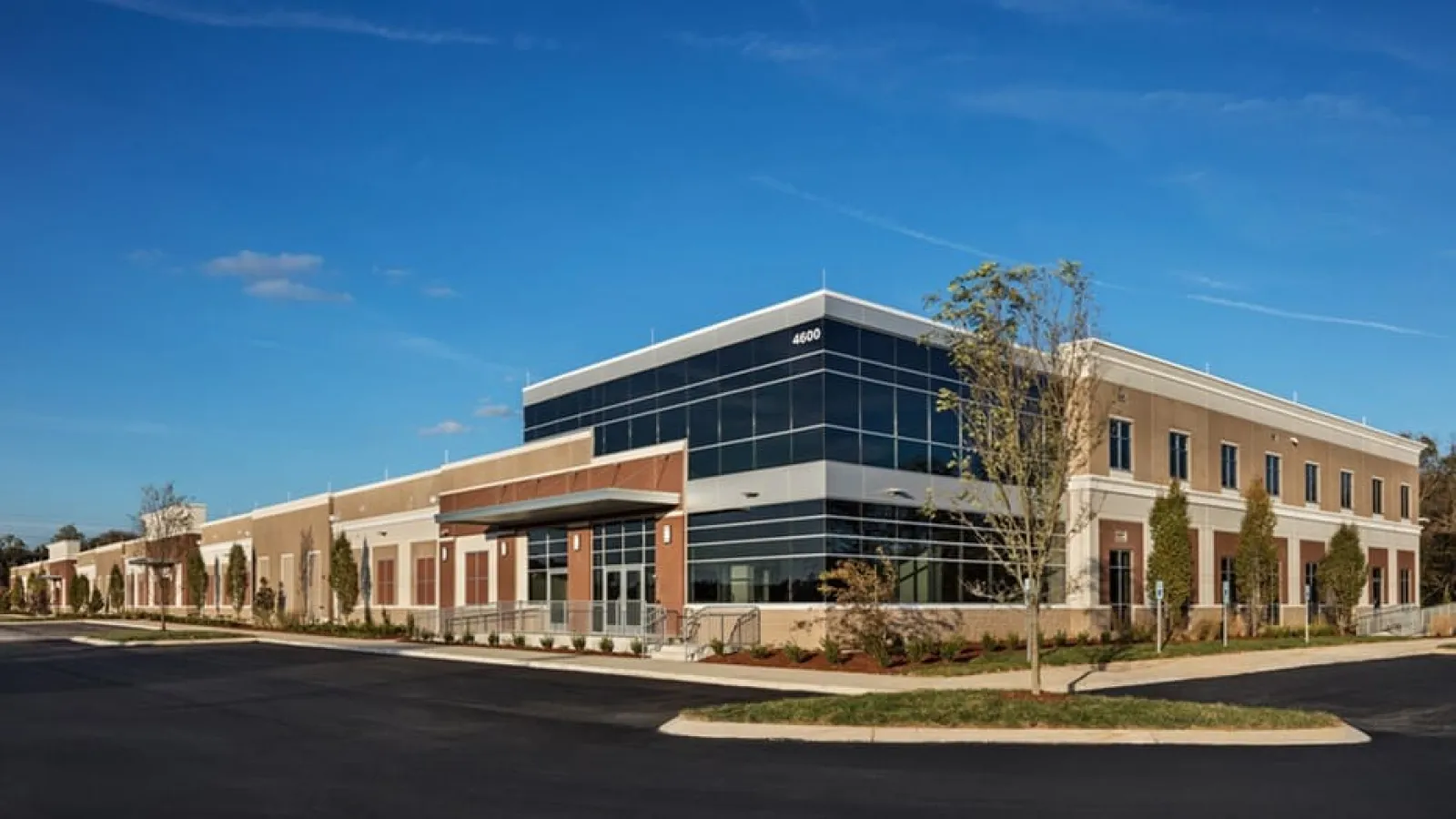 Modern commercial building with glass and brick facade under a clear blue sky in a landscaped area.