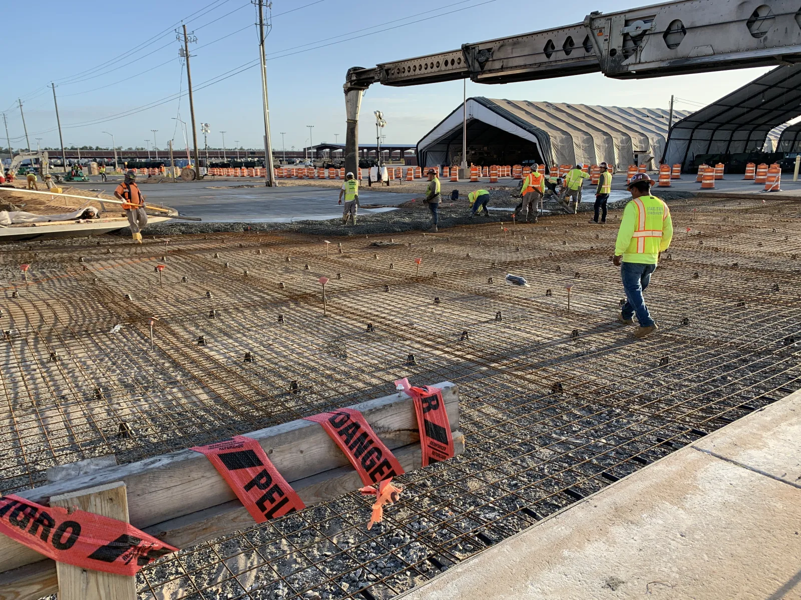 Construction workers in safety vests preparing a reinforced concrete foundation with rebar and pouring concrete onsite.