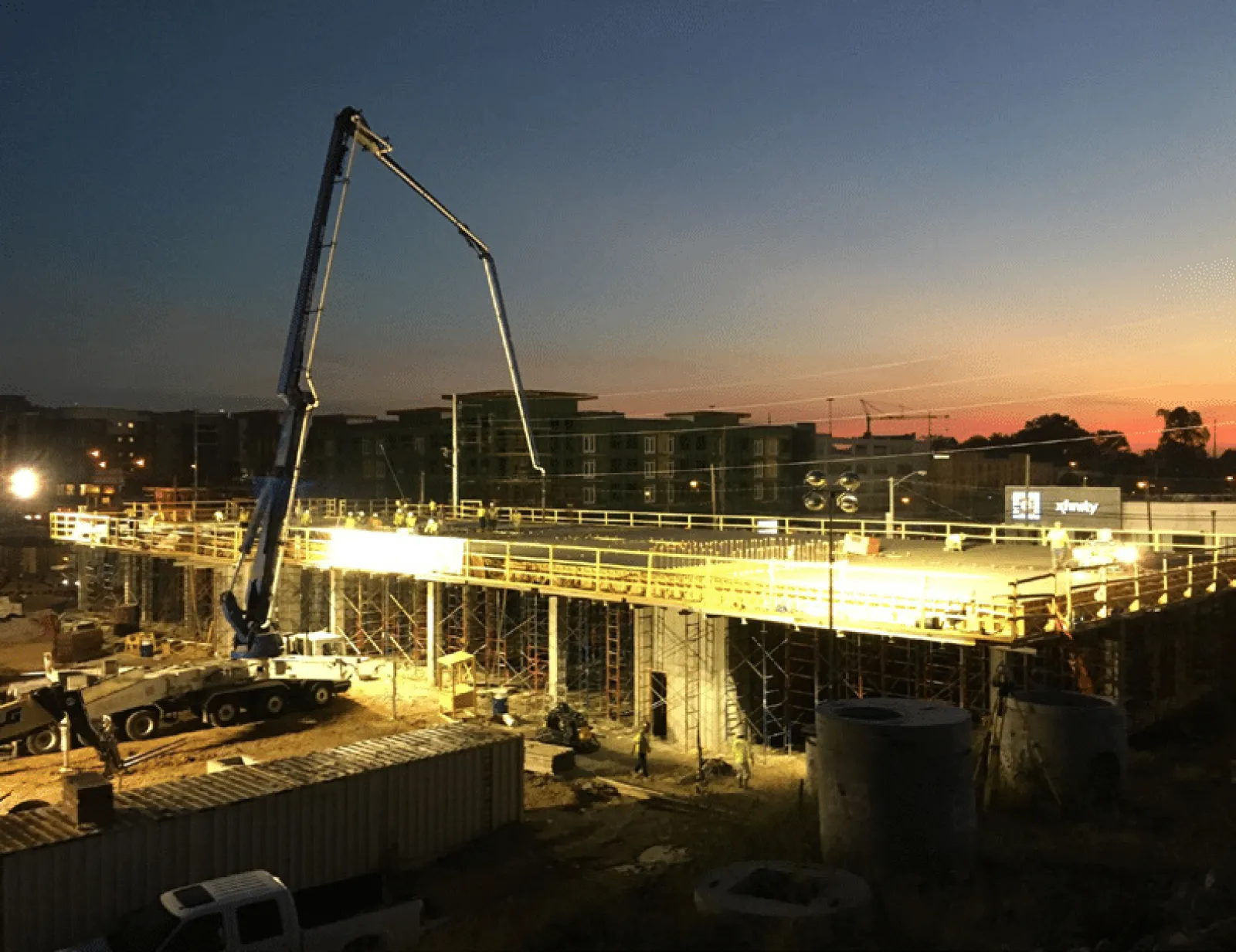 Nighttime construction site with workers and machinery building a large concrete structure under bright lights.