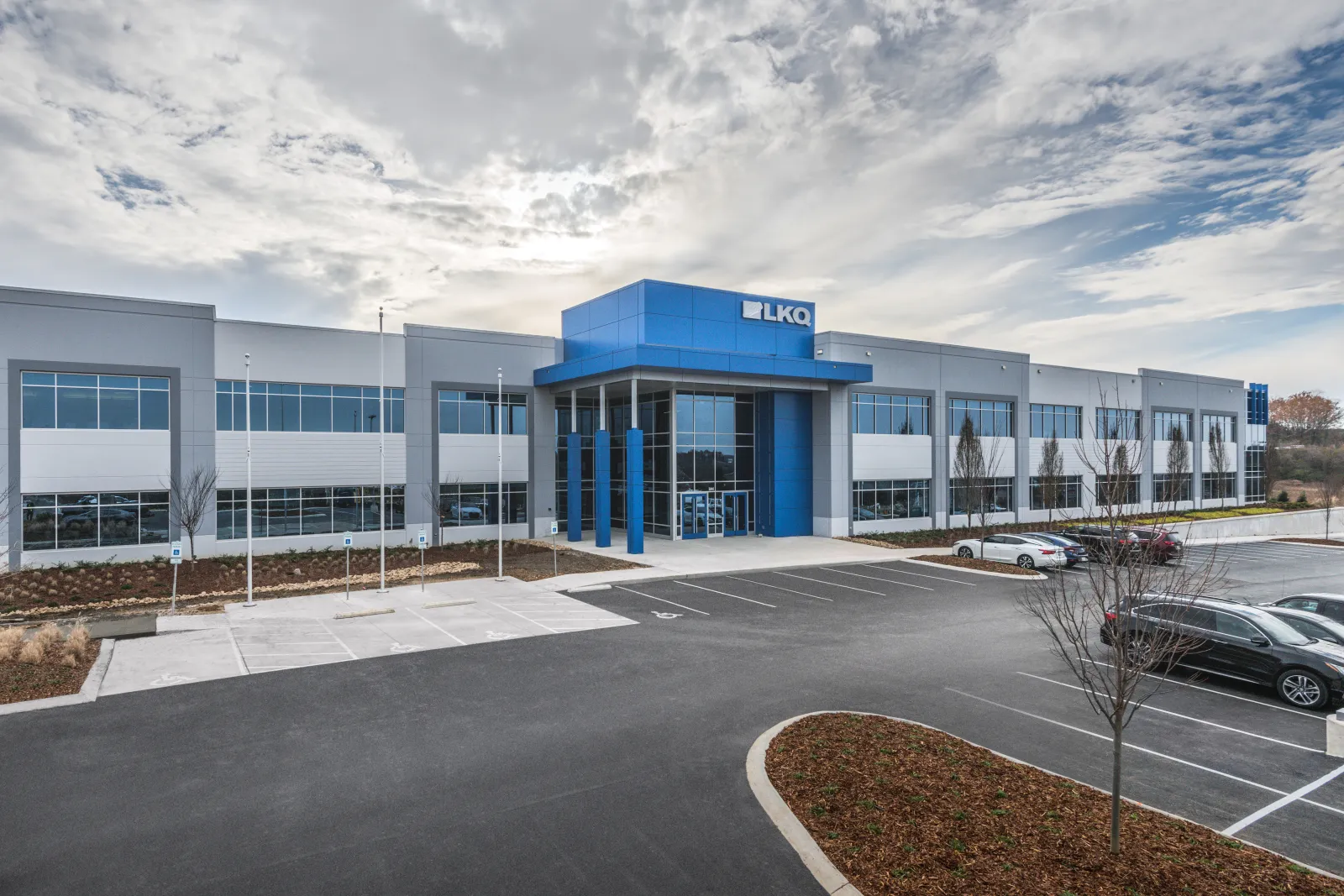 Modern LKQ corporate office building with large glass entrance and ample parking under cloudy sky.