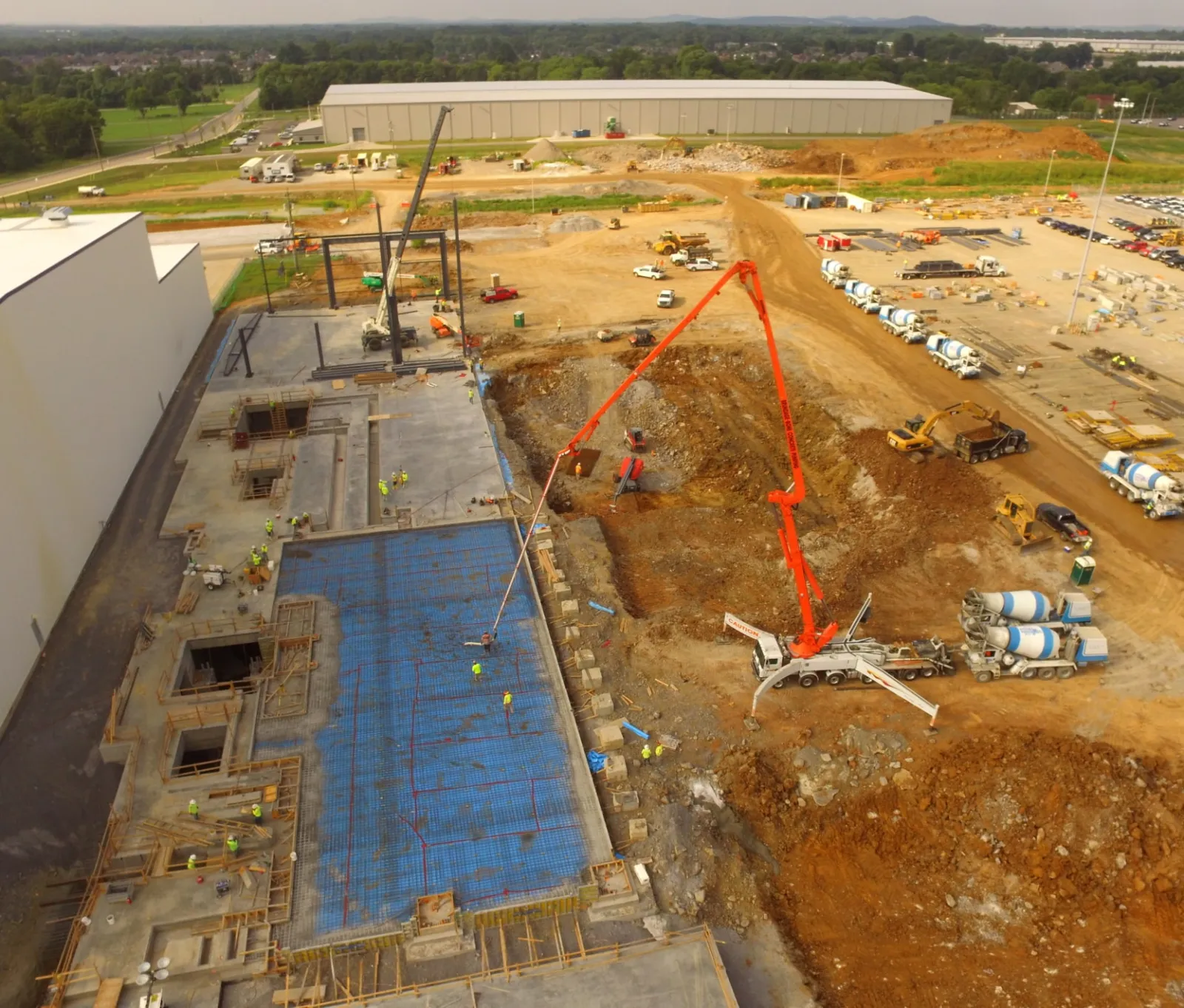 Aerial view of a construction site with concrete pouring, heavy machinery, and workers on site near industrial buildings.
