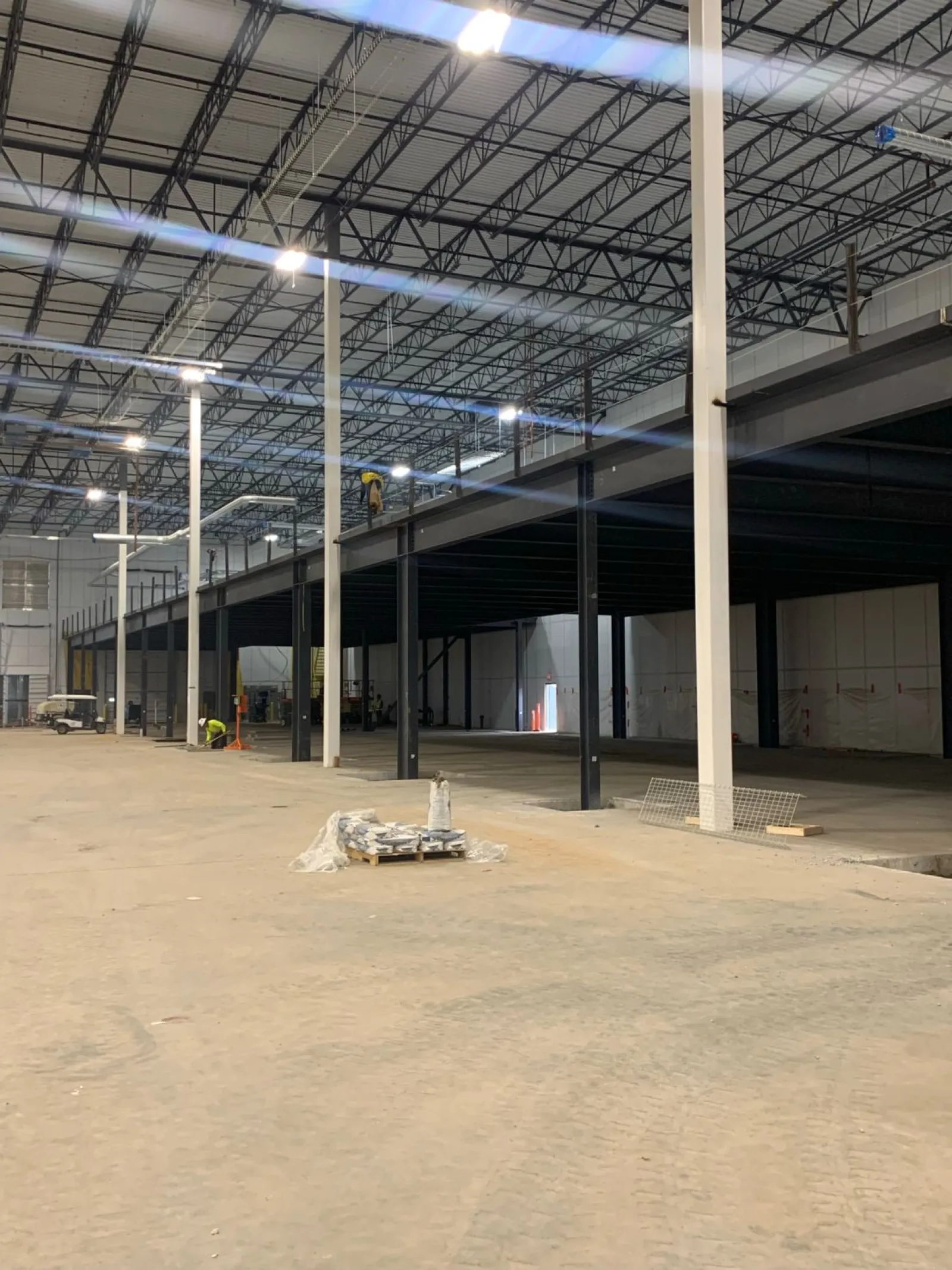 Large industrial warehouse under construction with steel framework and workers installing mezzanine level