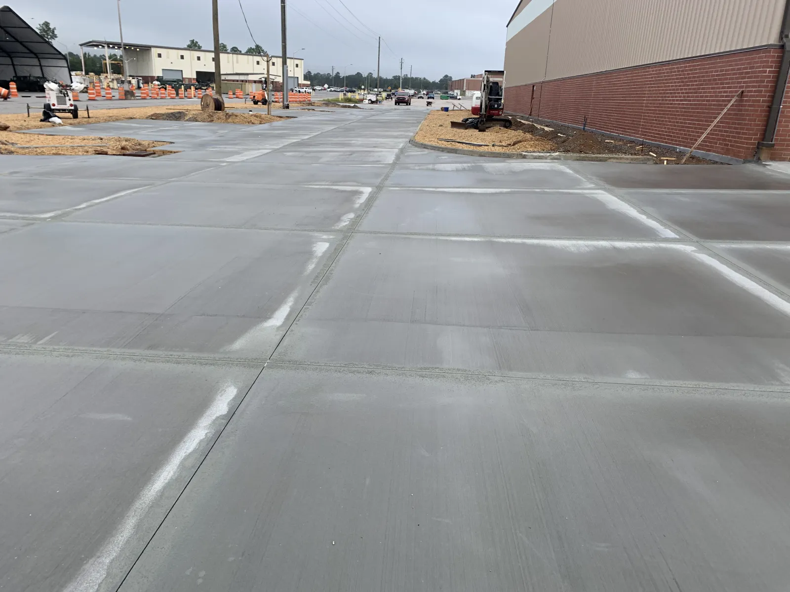 Freshly poured concrete pavement in an industrial area near a brick building and construction site.
