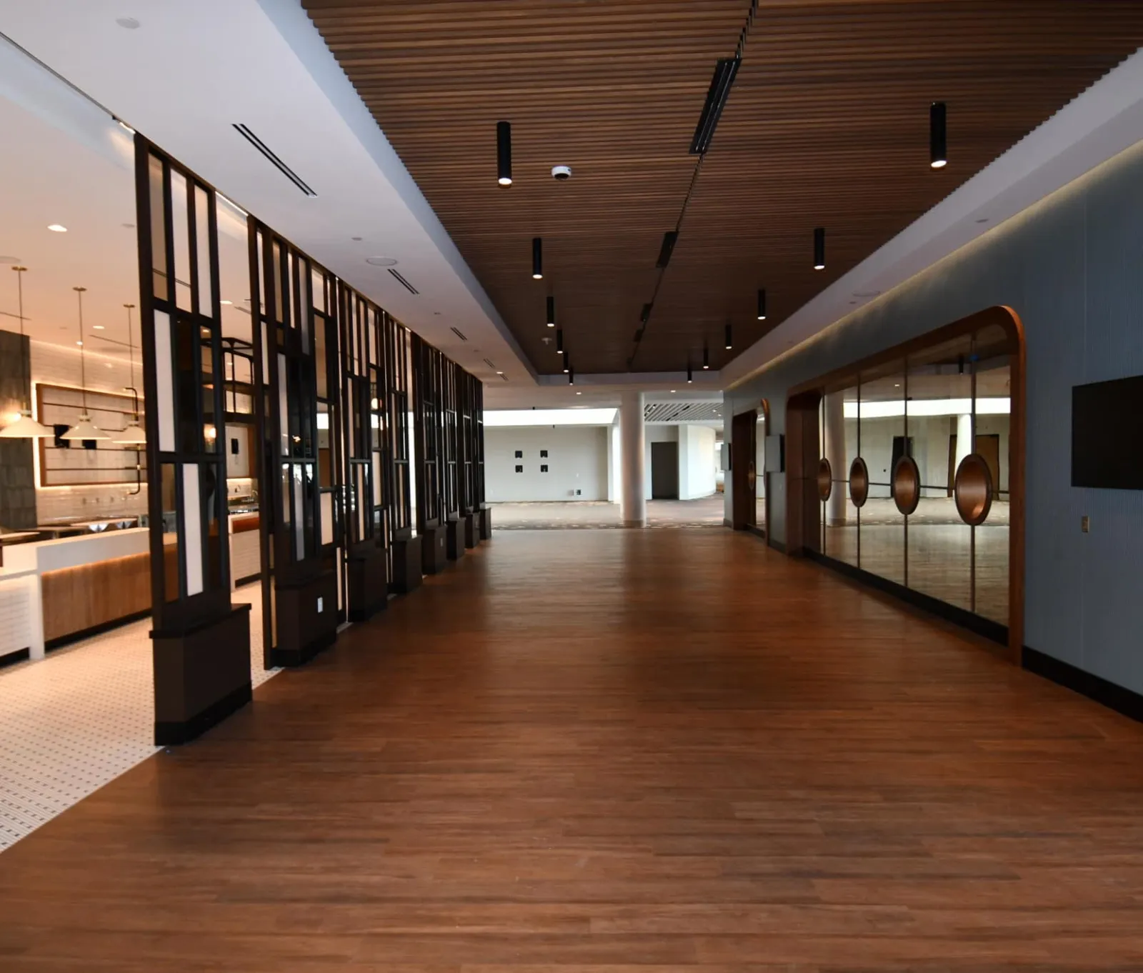 Spacious modern hallway with wooden flooring, slatted ceiling, decorative black partitions, and glass wall accents.