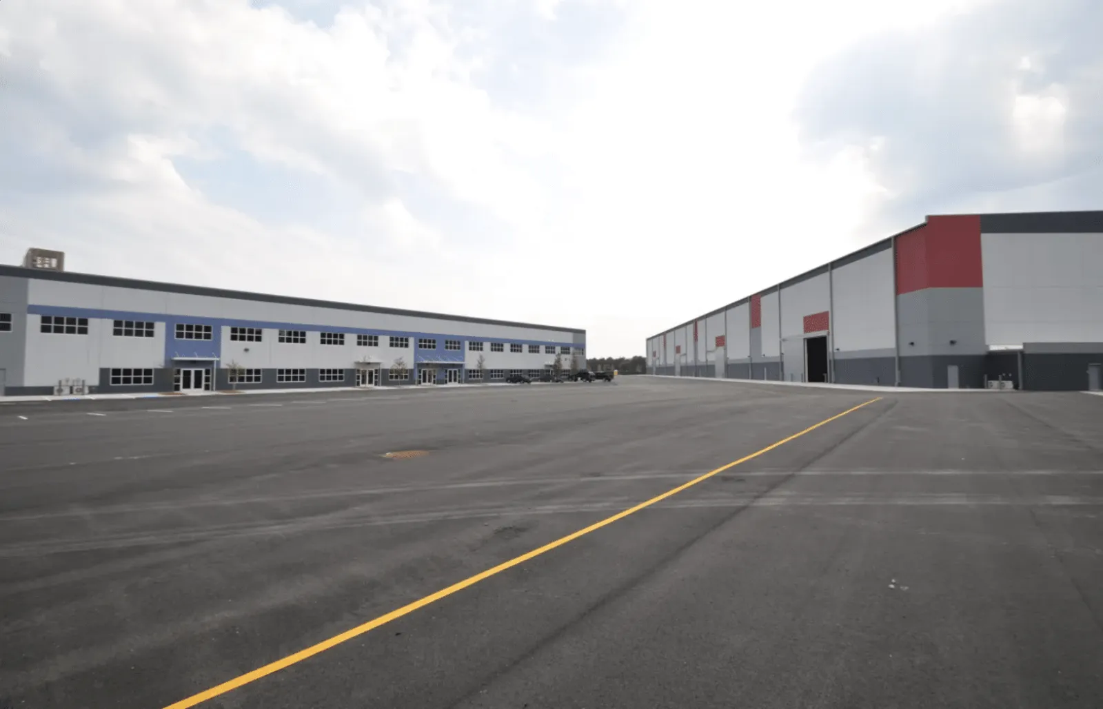 Wide view of a large industrial complex with two modern warehouse buildings and an expansive empty parking lot
