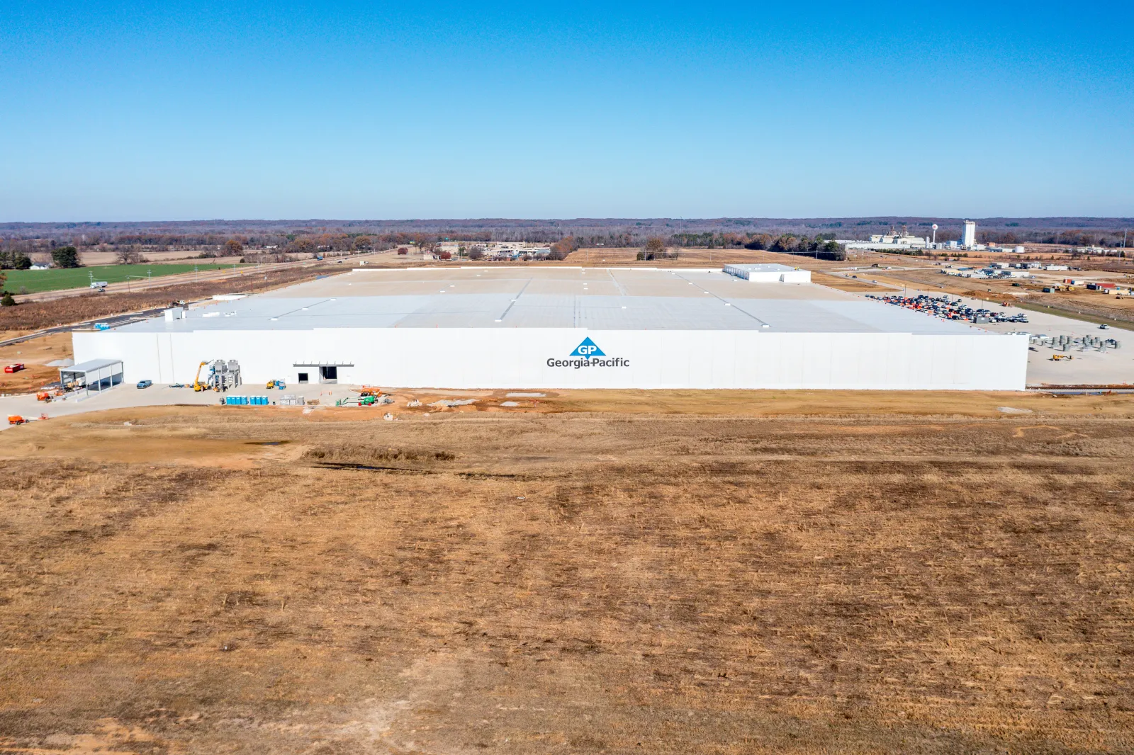 Large white Georgia-Pacific factory building in a rural area under clear blue sky with surrounding farmland.