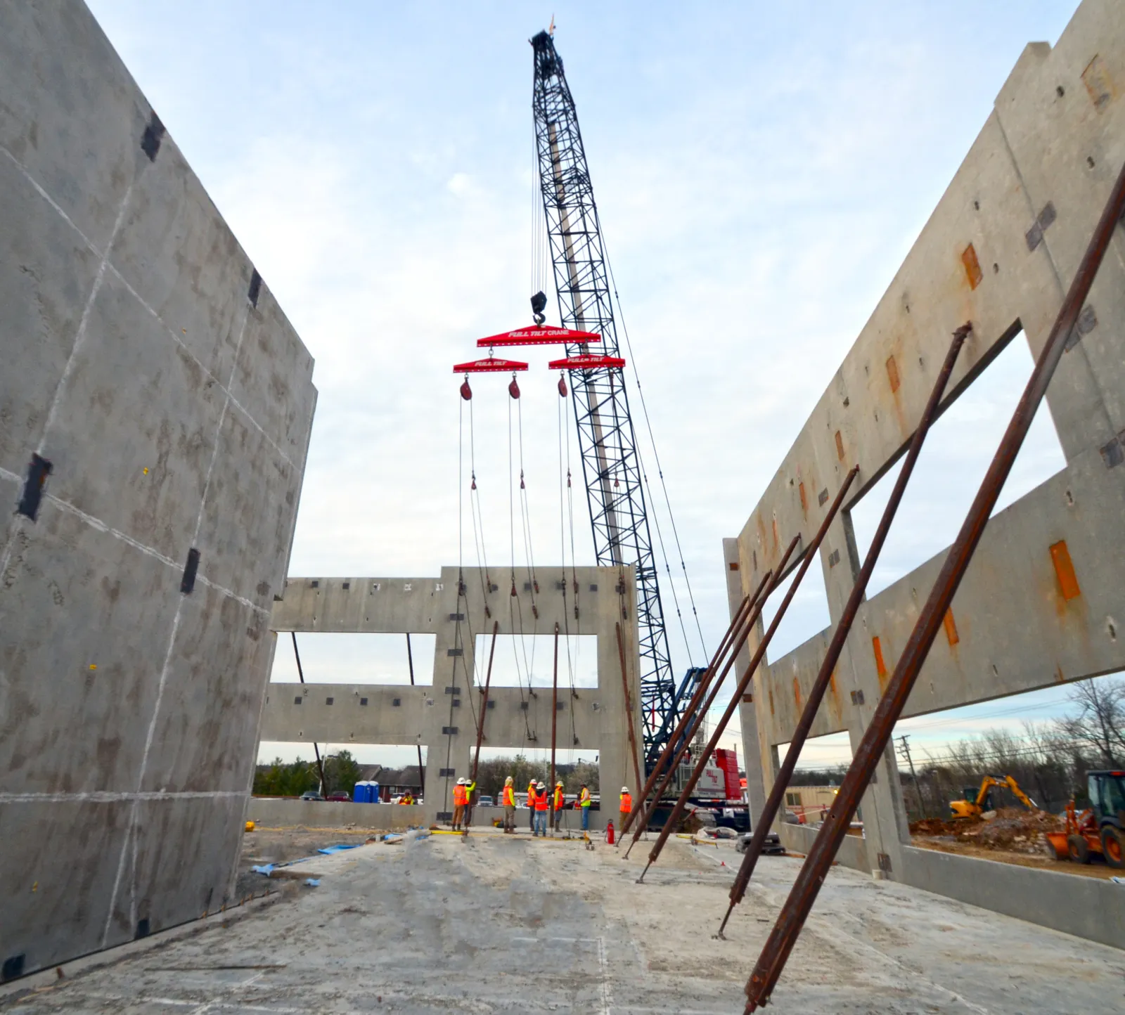 Construction workers assemble concrete walls with a large crane on an open building site.