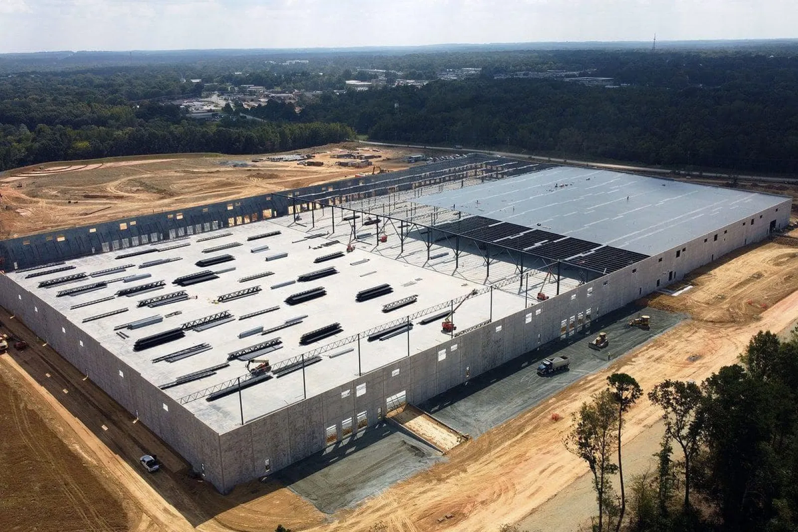 Aerial view of large warehouse under construction with steel framework and concrete walls in a clearing.