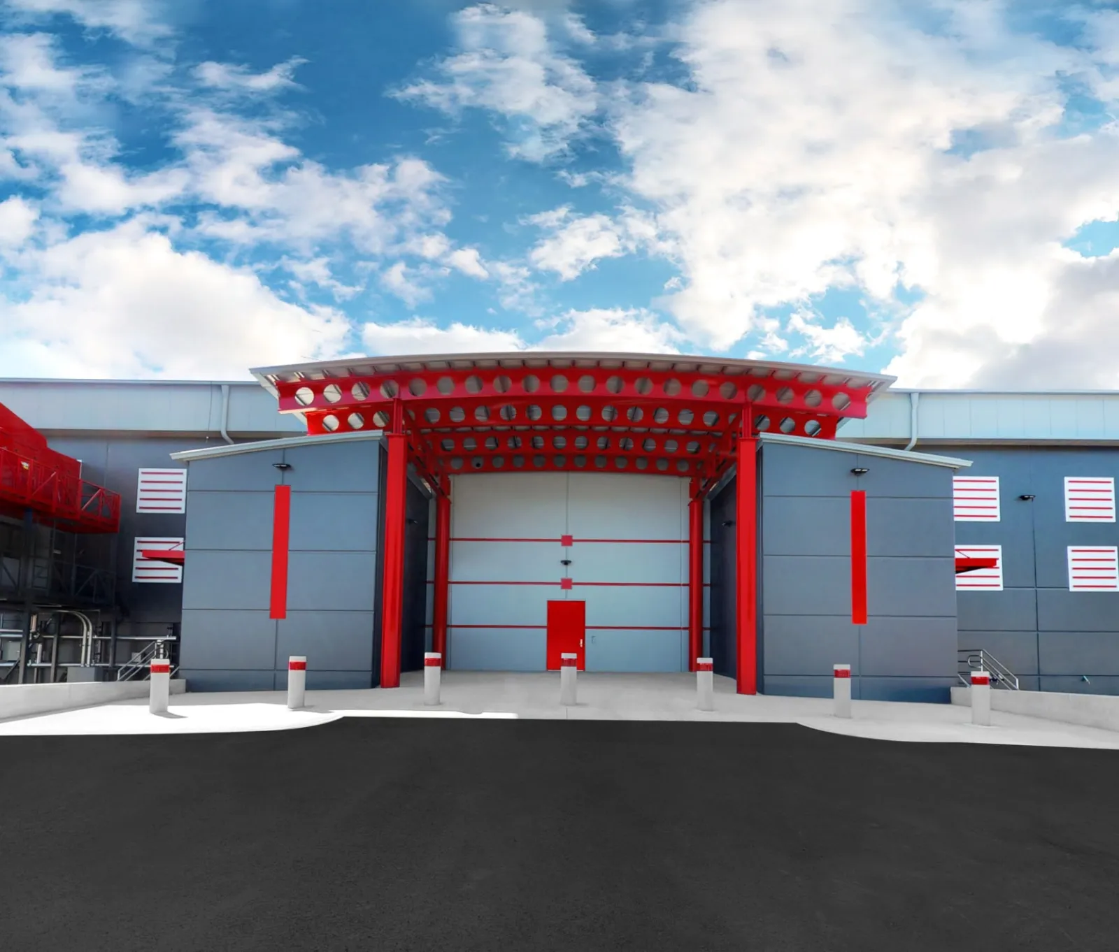 Modern industrial building facade with large gray and red entrance under partly cloudy blue sky.