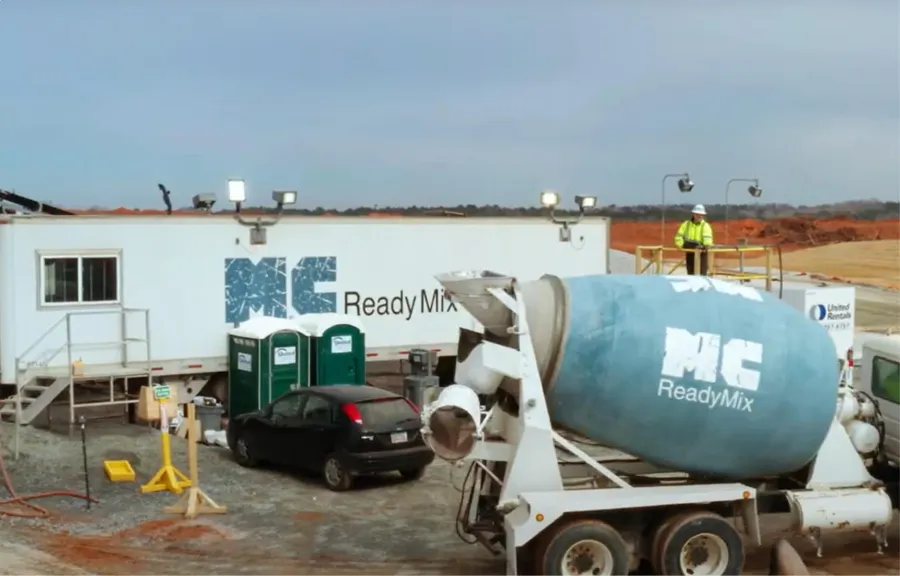 Concrete mixer truck and construction site with portable toilets and a company trailer in the background