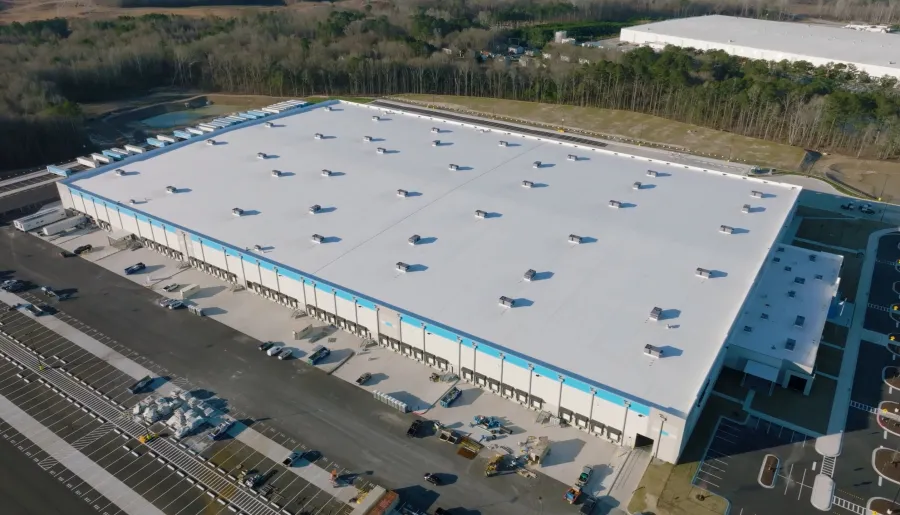 Aerial view of a large white industrial warehouse with loading docks and surrounding parking area.