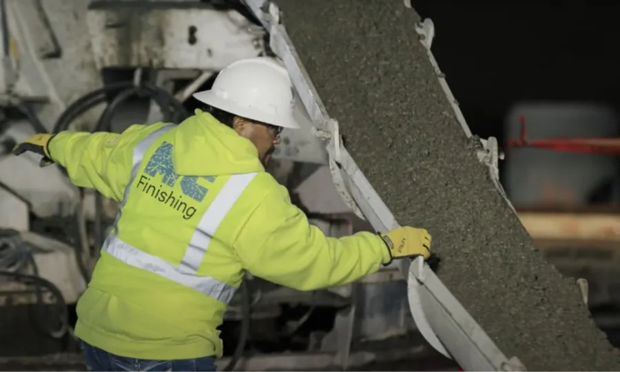 Construction worker in safety gear guiding fresh concrete from a chute at night on a building site.